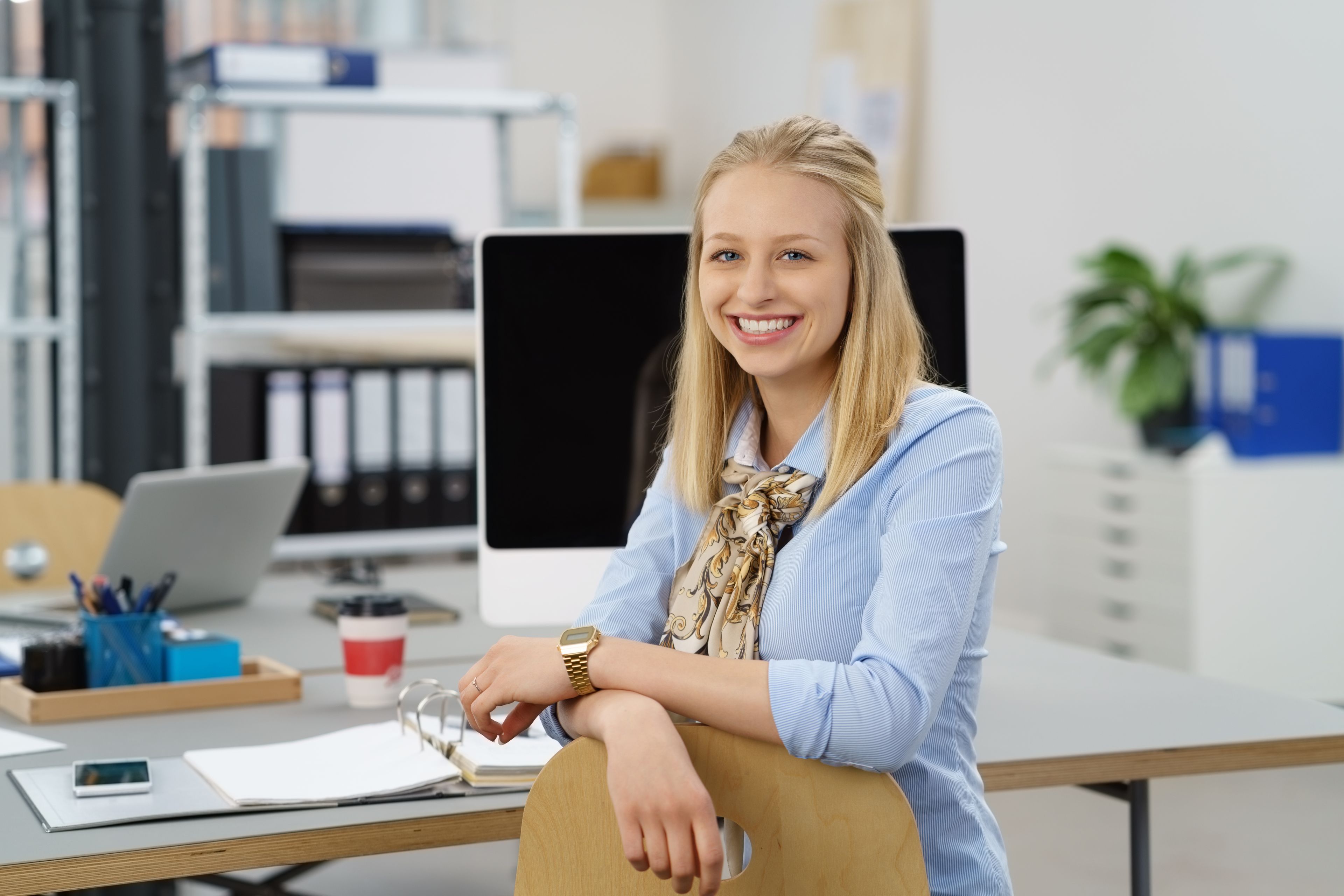 Freundliche Mitarbeiterin an modernem Arbeitsplatz im Büro mit Computer und Unterlagen.