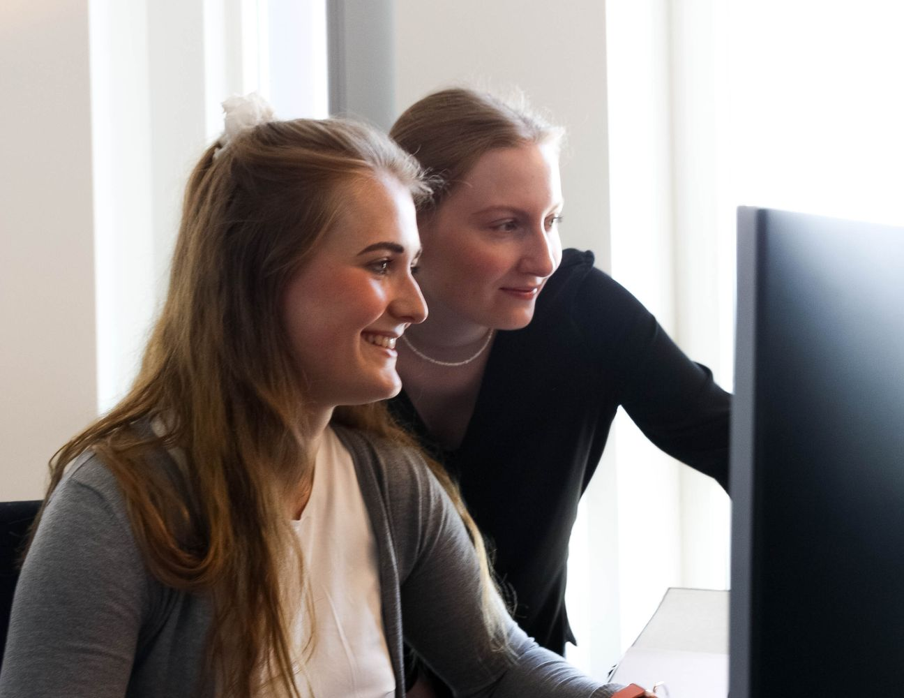 2 Frauen bearbeiten ein Projekt gemeinsam an einem Bildschirm.