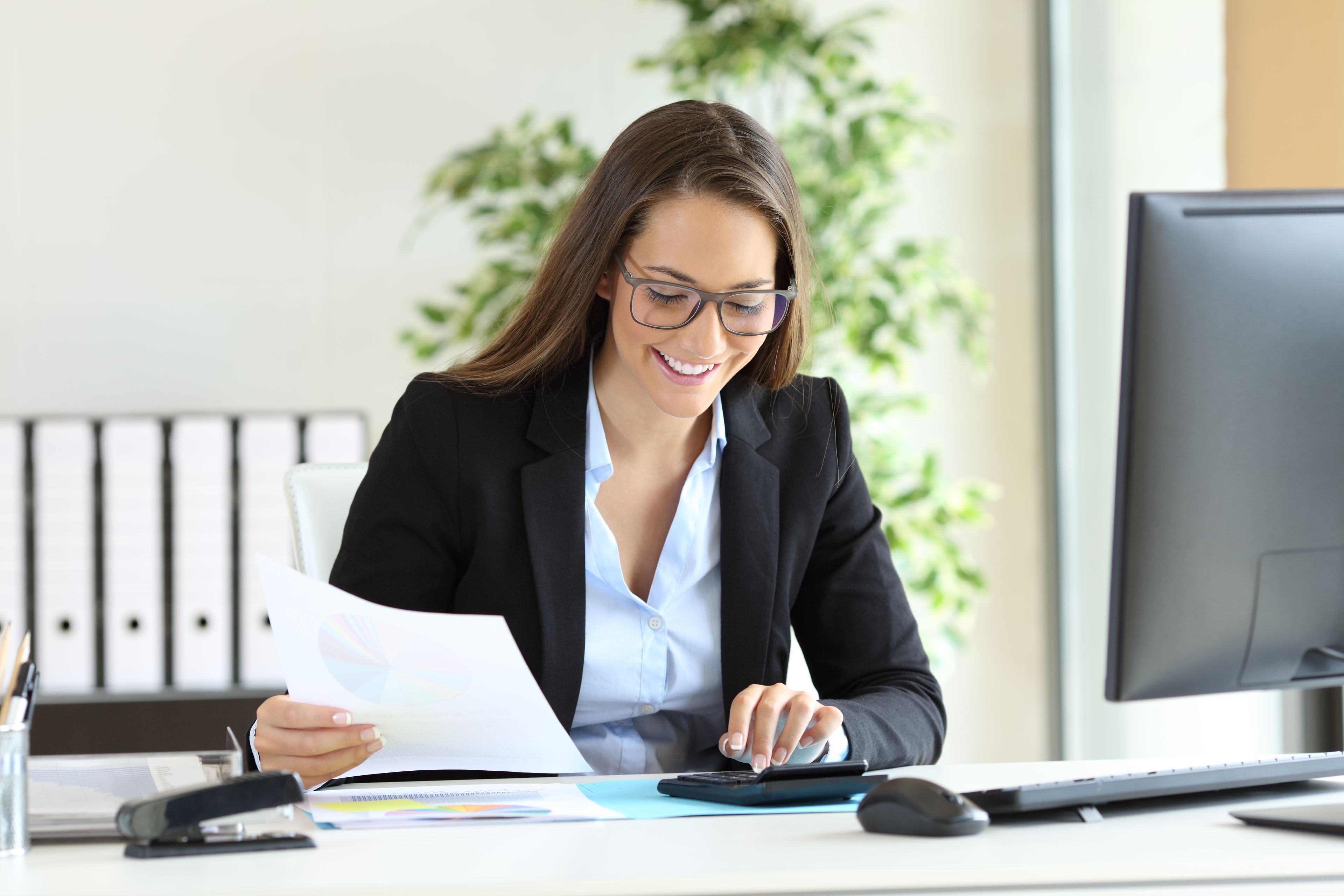 Freundliche Geschäftsfrau bei der Büroarbeit mit Unterlagen und Taschenrechner am modernen Arbeitsplatz.