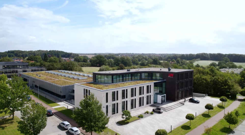 Luftaufnahme der modernen Unternehmenszentrale mit begrünter Dachfläche und großzügigem Bürogebäude in naturnaher Umgebung.