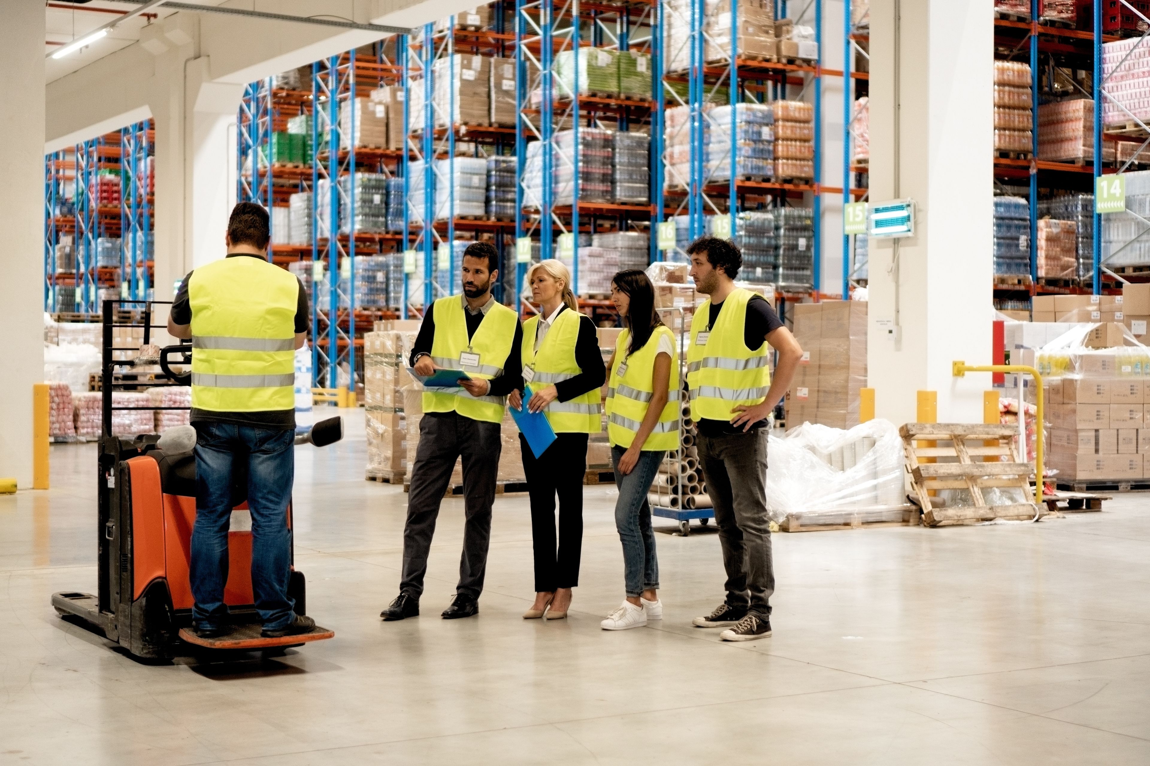 Mitarbeitende mit Warnwesten bei einer Besprechung in moderner Lager- und Logistikumgebung.