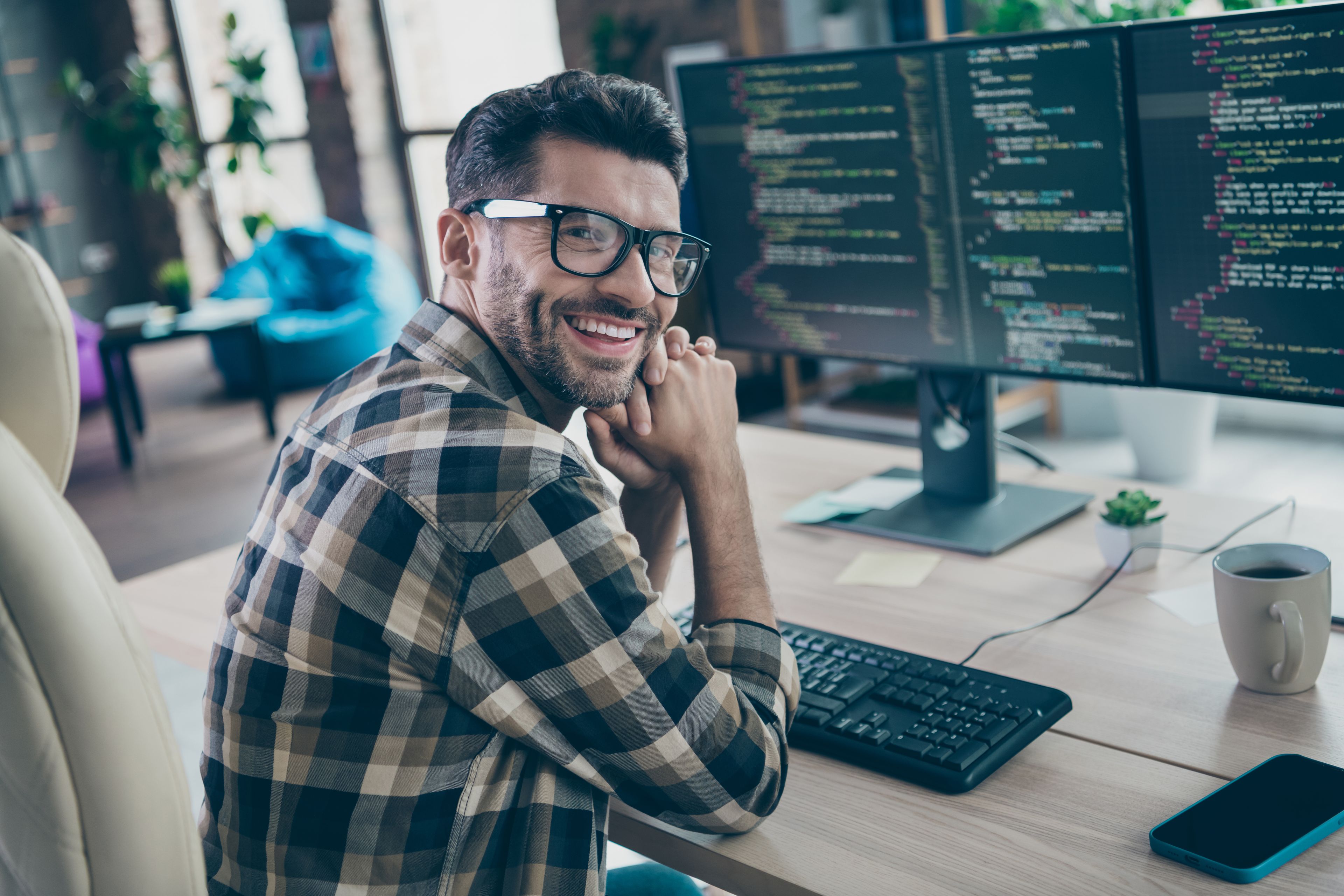 Freundlicher Softwareentwickler arbeitet an mehreren Bildschirmen mit Programmcode in moderner Büroumgebung.