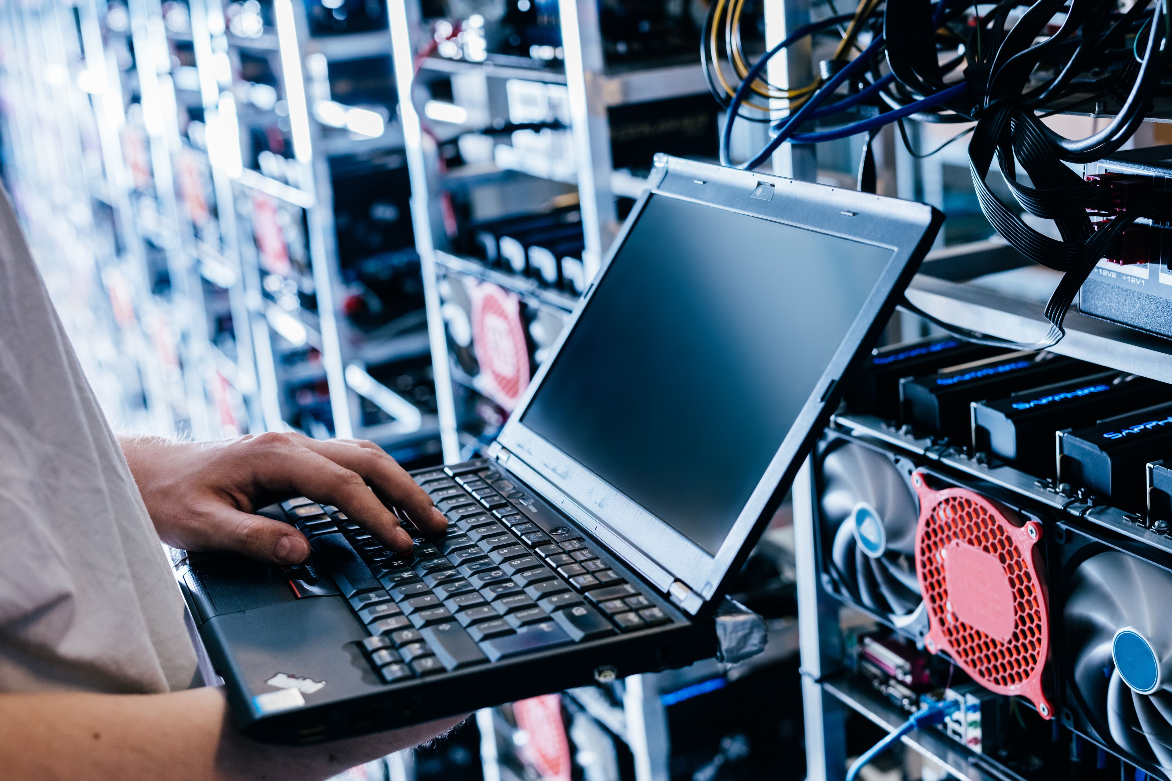 IT-Techniker arbeitet mit Laptop an Server- und Netzwerktechnik in moderner Rechenzentrumsumgebung.